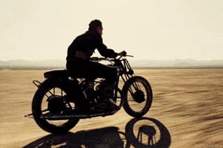 Un motard traverse un vaste terrain ouvert, sans casque, inspirant la liberté.