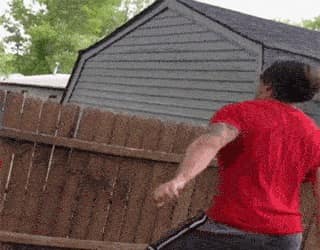 Une personne tente de sauter au-dessus d'une barrière de jardin en bois et se vautre.