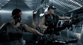 Vasquez du film Aliens tient une mitrailleuse lourde pointée devant elle, puis la lève pour être le long de son torse, avec son équipier qui effectue le même mouvement derrière elle.