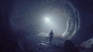 Notre protagoniste traverse une caverne naturelle et sombre pleine de stalactites, avec une seule lumière artificielle qui éclaire son chemin.
