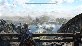 Kratos, en haut d'une montagne, de jour, contemple un lac entouré de verdure, avec une énorme statue d'un Nain au loin et une île au centre qui abrite quelques bâtiments. L'^le et l'ensemble de la région au loin semblent enveloppés dans une fine couche de brume.