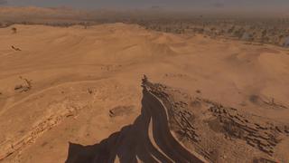 Vue éloignée en plongée sur Basim qui se tient sur le bord d'une falaise, surplombant le désert.
