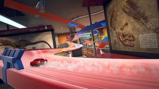 Une voiture miniature traverse en dérapant un circuit dans une pièce de musée centrée autour de dinosaures.