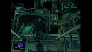 Solid Snake se tient face à la caméra, en arrière plan nous pouvons voir un hangar qui contient Metal Gear REX.